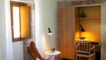 Een gezellige kamer met houten vloer, een houten stoel, een klein rond tafeltje, een lamp en een raam met gordijnen.