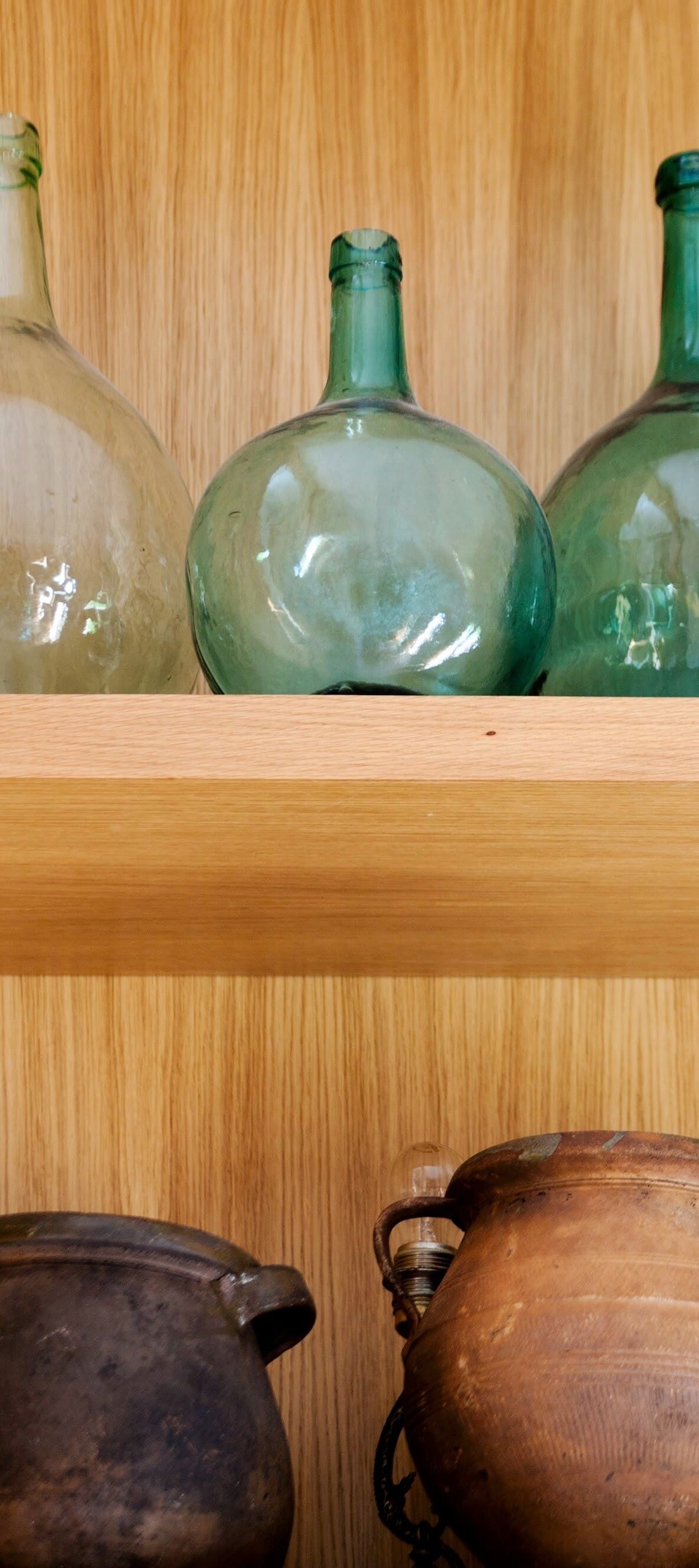 Una estantería de madera con botellas de vidrio y macetas de cerámica.