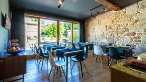 A restaurant with wooden tables and chairs, stone walls, and large windows. - Os Lambráns (Padron)