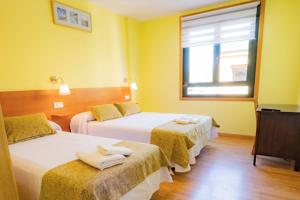 Une chambre d’hôtel avec trois lits, un plancher en bois et une fenêtre avec des stores.