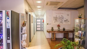 A hotel hallway with a reception desk, a map on the wall, and a bookshelf. - Hotel Ciudad de Alcalá (Alcala de Henares)
