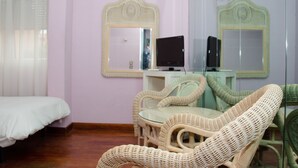 A room with a bed, wicker chairs, a small table, a television, and two mirrors on the wall. - Hotel Ciudad de Alcalá (Alcala de Henares)