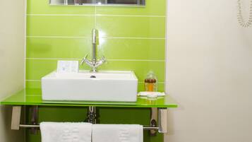 Un baño con pared de azulejos verdes, un lavamanos blanco, un espejo y un teléfono.