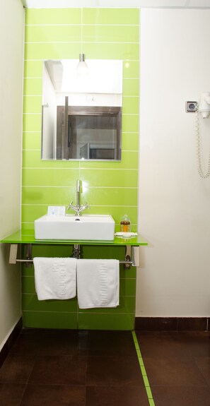 Um banheiro com parede revestida de azulejos verdes, pia branca, espelho e telefone.