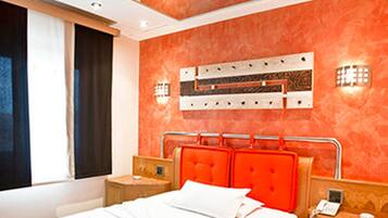 A modern hotel room with a large bed, orange headboard, and a ceiling with recessed lighting.