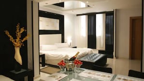 Una habitación de hotel moderna con una cama impecable, una mesita de noche con una botella de champán y una pequeña mesa con fruta y un menú.