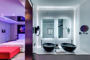 Un baño moderno con un espejo grande, dos lavamanos y un sofá rojo en la habitación contigua.