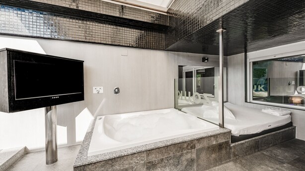 Un baño moderno con una bañera grande, un espejo y un televisor.