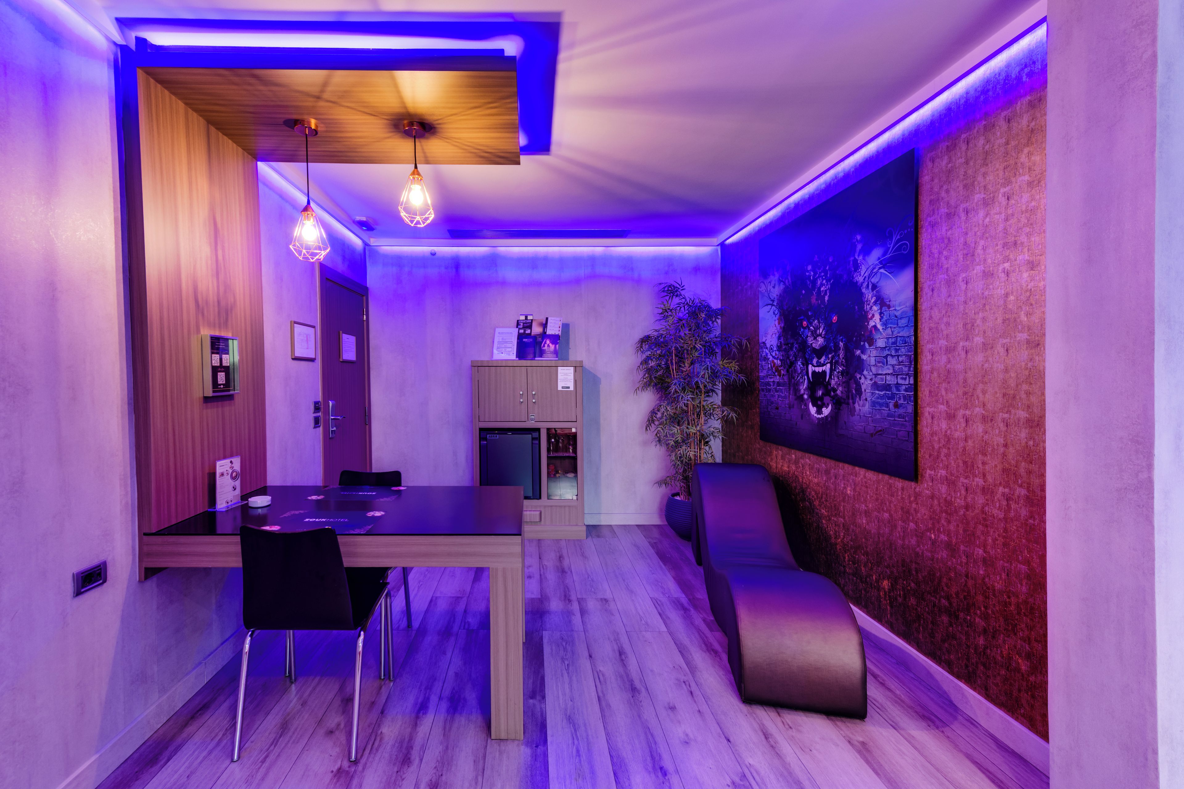Quarto moderno com mesa de jantar, cadeiras, pequena geladeira e televisão fixada na parede.