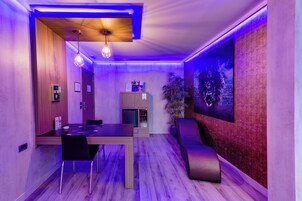 Una habitación moderna con mesa de comedor, sillas, un refrigerador pequeño y un televisor montado en la pared.