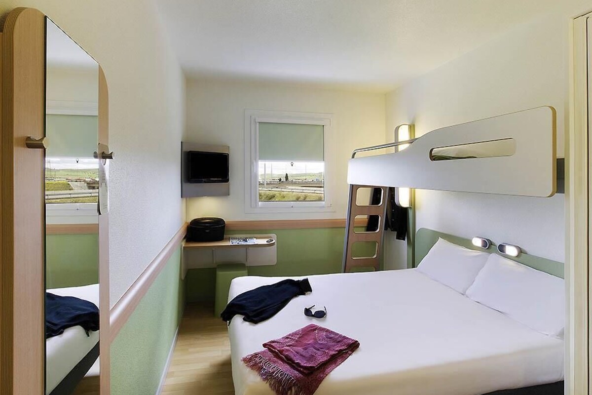A compact hotel room with a bunk bed, a small desk with a chair, a television, and a window with a view.