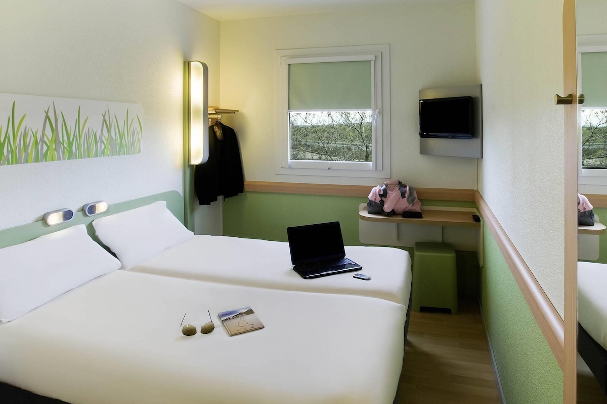 Une chambre d’hôtel avec un lit, un ordinateur portable, une fenêtre, une télévision et un miroir.