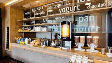 Mostrador de café con estantes que exhiben diferentes productos alimenticios como yogur, chocolate y pan.
