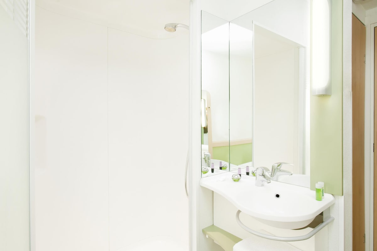 Un baño con lavamanos blanco, espejo y ducha.