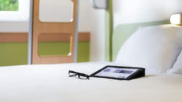 Uma cama com um tablet e óculos, uma parede verde e uma janela com vista.