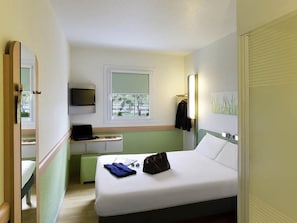 A hotel room with a bed, a desk with a laptop, a TV, and a window with a view of trees. - Ibis Budget Madrid Getafe (Getafe)