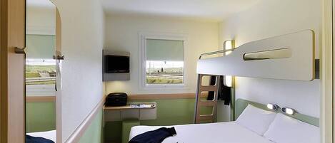 Habitación de hotel pequeña con una cama litera, un escritorio y una silla, un televisor y una ventana con vistas.