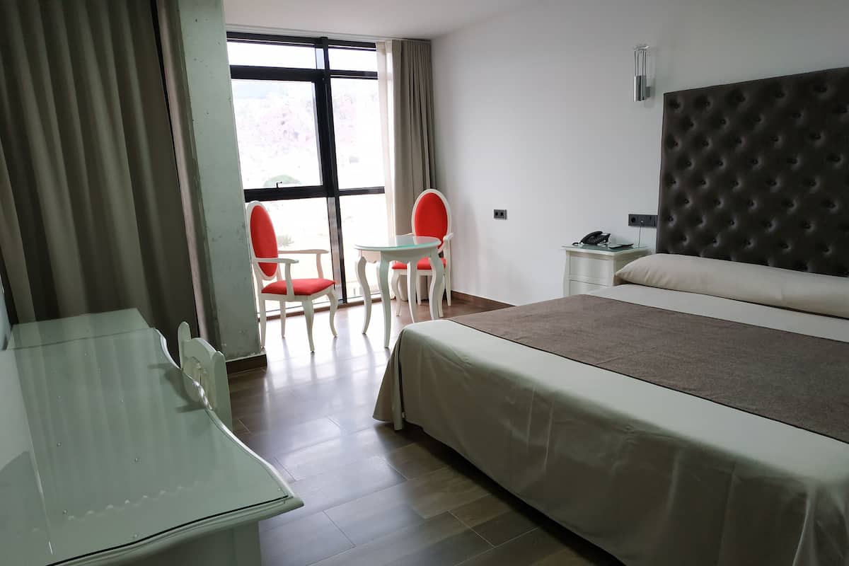 Habitación de hotel con cama, escritorio, dos sillas, una mesita y ventana con cortinas.