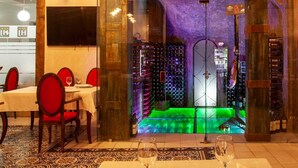 Un restaurante con una división de vidrio, sillas rojas, una mesa con copas de vino y una estantería para vinos al fondo.