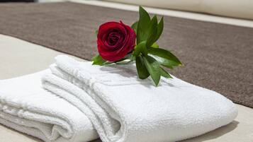 Una toalla blanca doblada con un rosal rojo sobre la cama.