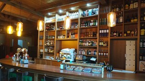 Zona de bar con estantes llenos de botellas de licor, una máquina de café y taburetes de bar.