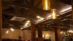 Un interior espacioso con vigas de madera a la vista, lámparas colgantes y una zona de bar con grifo de cerveza.