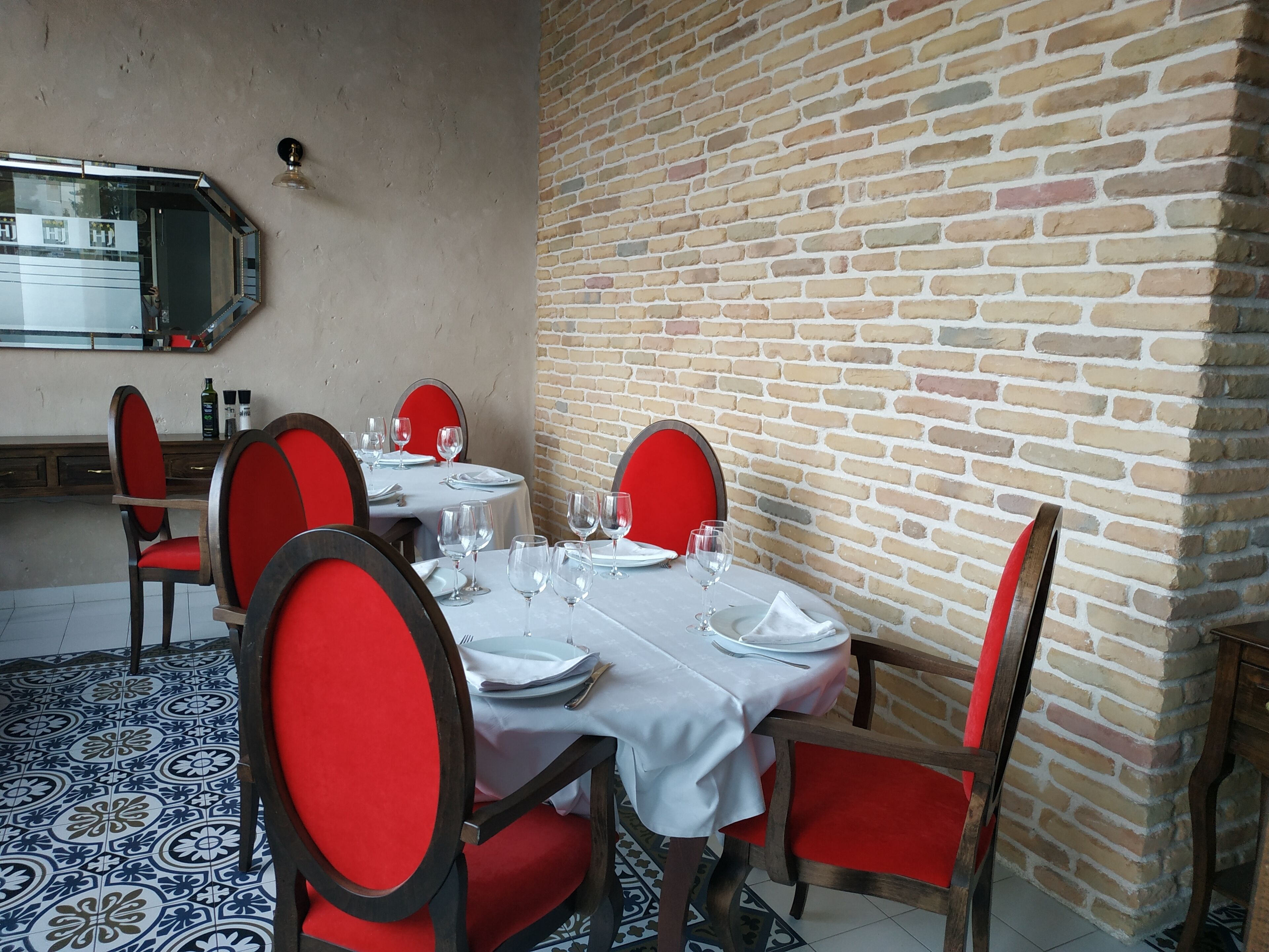 A dining area with a brick wall, red chairs, and a tiled floor.