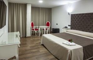 A hotel room with a bed, a desk, a chair, a small table, and a nightstand. - Hotel Julián (Alhama de Murcia)