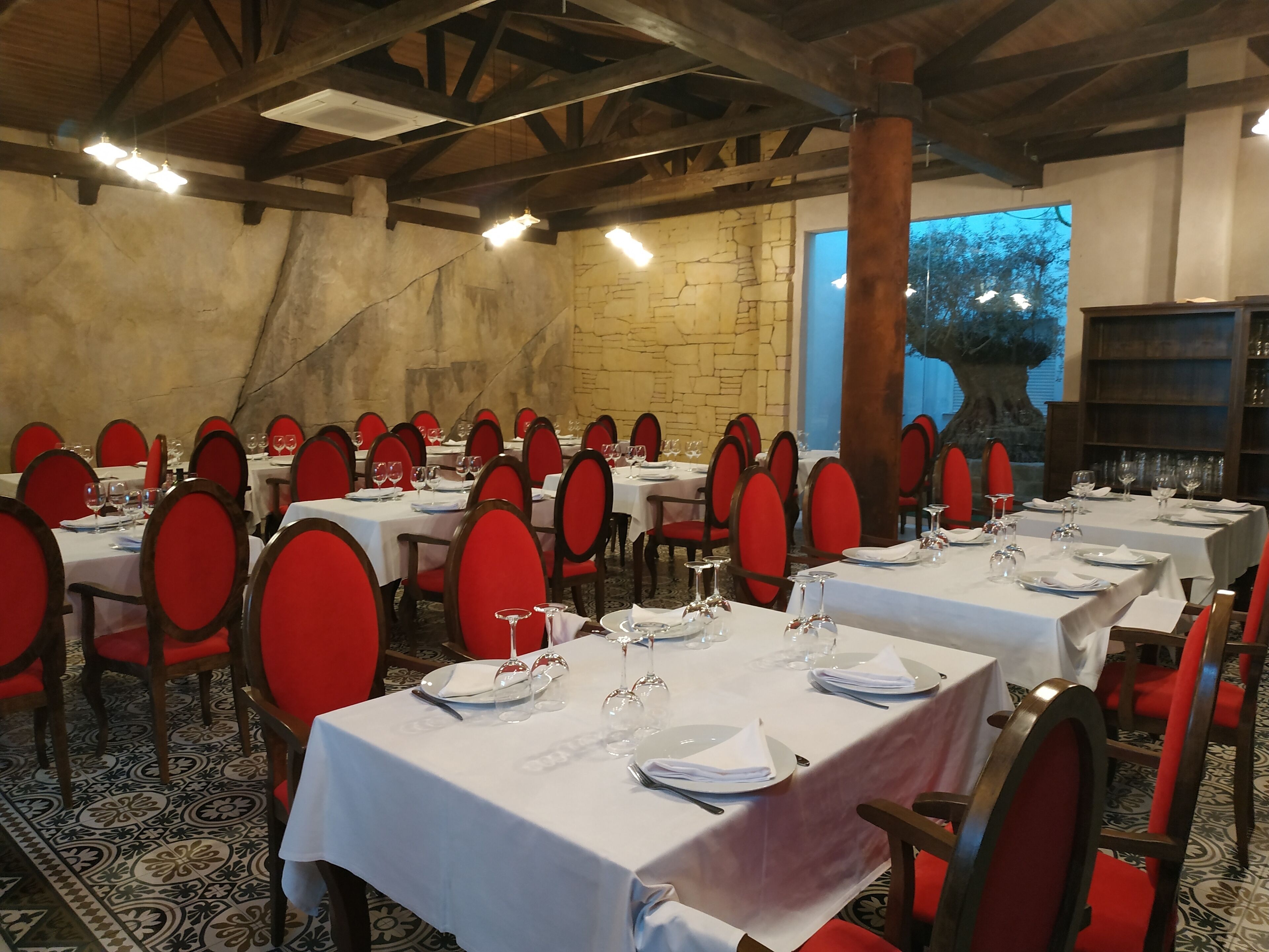 Un restaurante con varias mesas dispuestas para comer, con sillas rojas y manteles blancos.