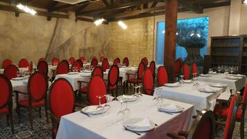 Un restaurante con varias mesas dispuestas para comer, con sillas rojas y manteles blancos.