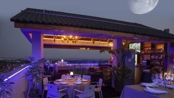Un área de comedor al aire libre con mesas dispuestas para una comida, un bar con estantes llenos de botellas y vista a la luna.