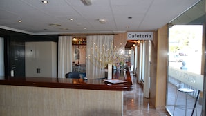 A hotel lobby with a reception desk, a sign reading "Cafeteria," and a view of the outside through large windows. - Hotel Venta el Puerto (Murcia)