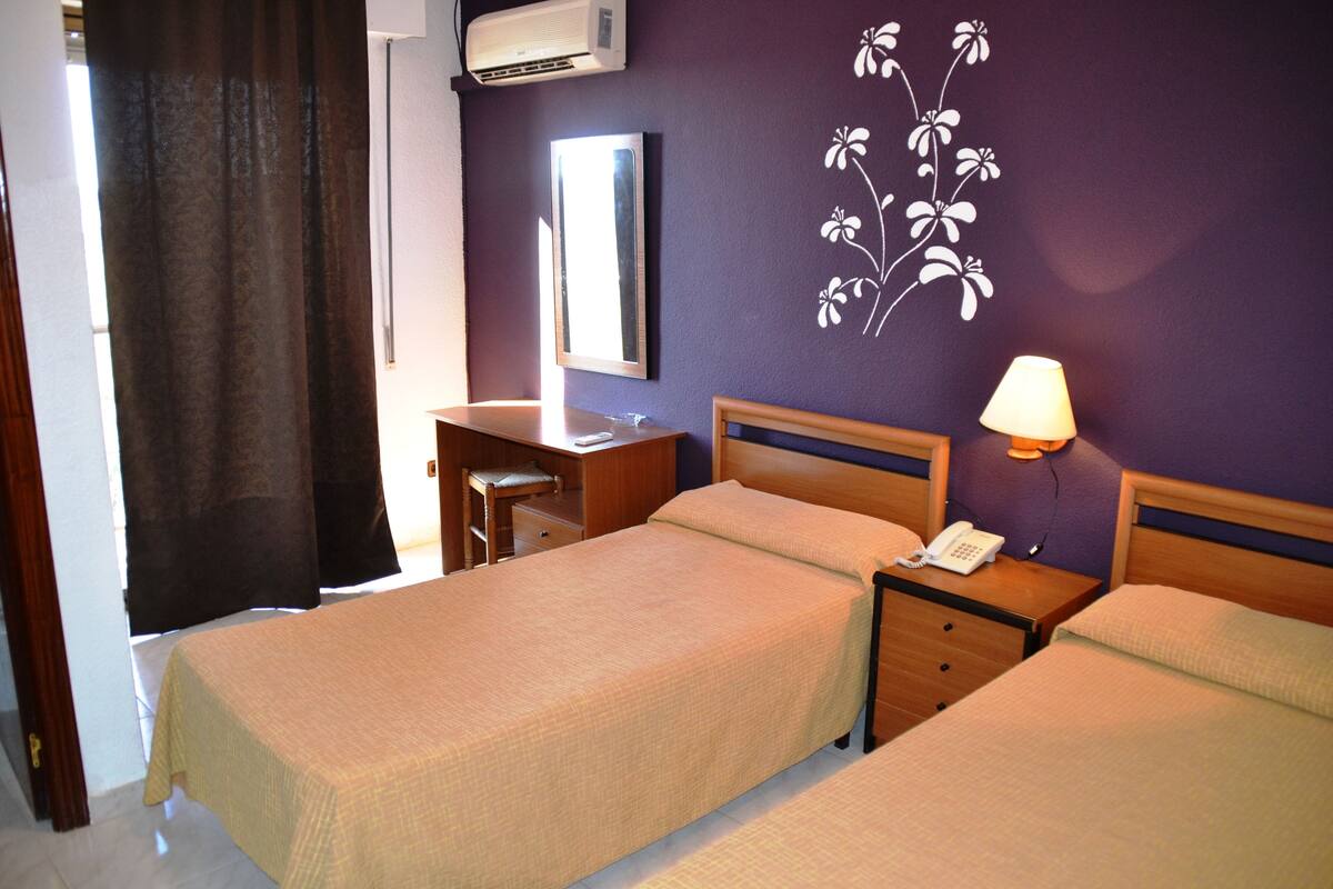 A hotel room with two beds, a desk, a chair, a lamp, and a mirror.