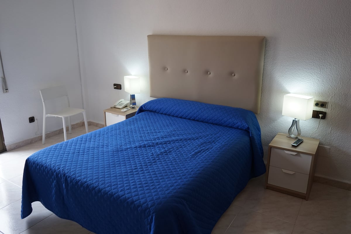 A hotel room with a large bed, two bedside tables, a chair, and a wall-mounted phone.