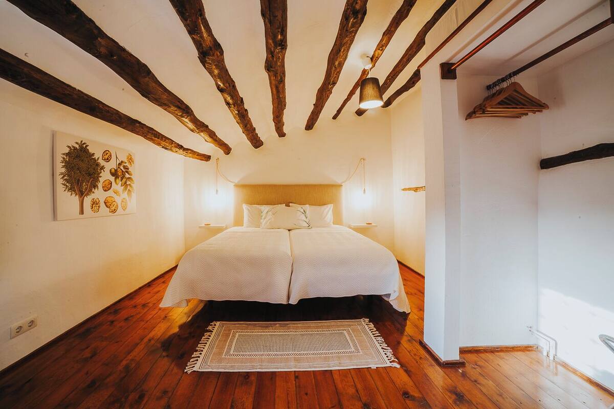 Un dormitorio con techo de madera, una cama con ropa de cama blanca, una lámpara de pared y una alfombra.
