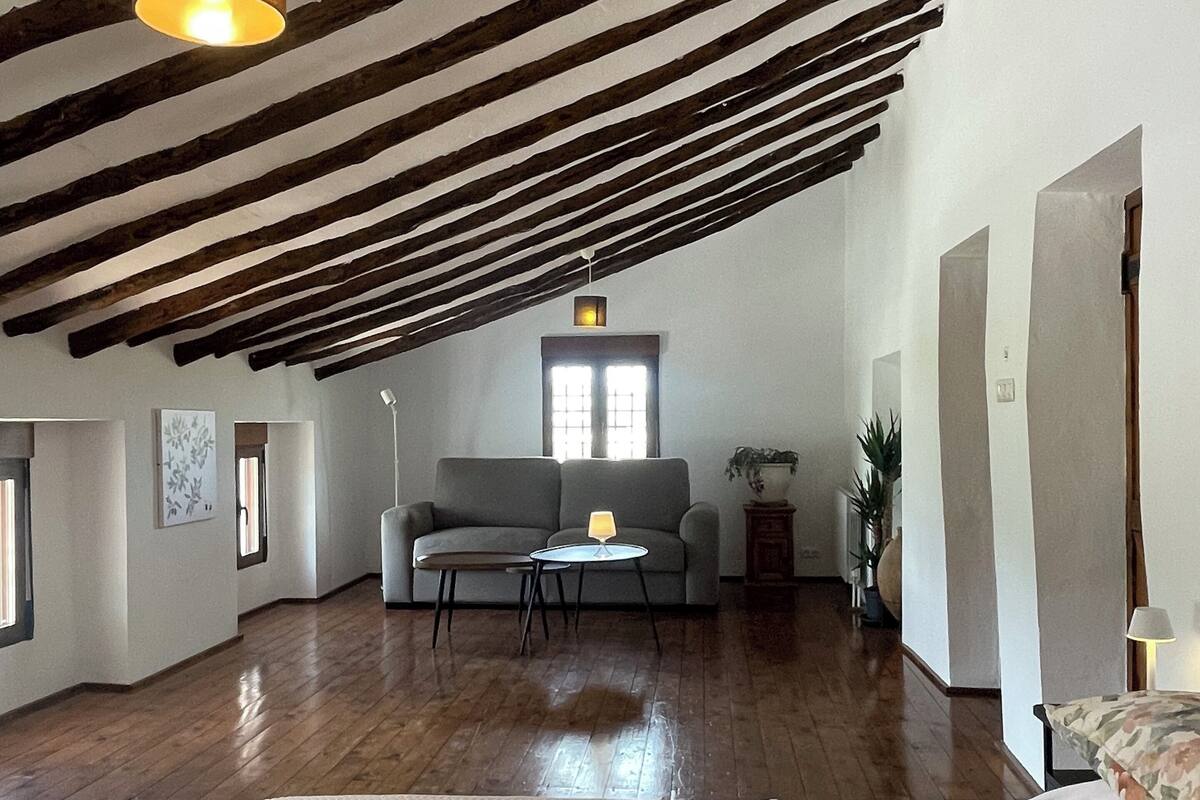 Una habitación amplia con vigas de madera a la vista, un sofá, una mesita y una cama con ropa de cama estampada.