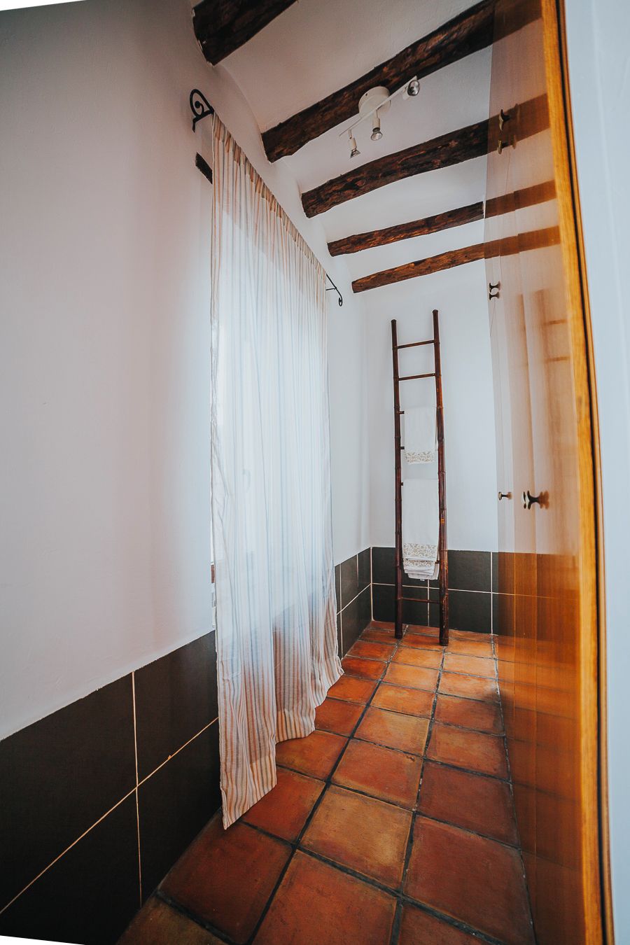 A narrow hallway with a tiled floor, a wooden ladder leaning against the wall, and a white curtain partially drawn to the side.