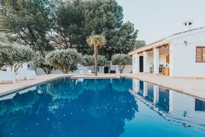 A swimming pool with clear blue water, surrounded by white lounge chairs and trees. - Casa Pedro Barrera (Caravaca de la Cruz)