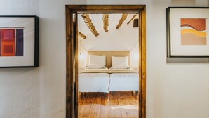 Un umbral que da a una habitación con cama, suelo de madera y techo con vigas a la vista.