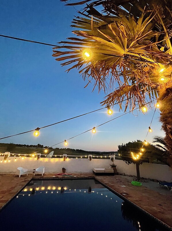 Un espace piscine agrémenté de guirlandes lumineuses, de chaises longues et offrant une vue dégagée sur le paysage.