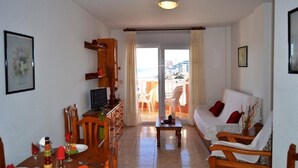 A living room with a sofa, a dining table with chairs, a TV, and a view of the outside. - Hawaii 6 (La Manga)