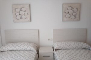 Una habitación con dos camas, cada una con una colcha estampada y almohadas a juego. Hay dos obras de arte en la pared que representan diseños abstractos.