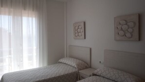 A bedroom with two beds, a window with sheer curtains, and two wall-mounted artworks. - Vistamar (San Javier)