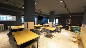 A modern restaurant interior with multiple dining tables and chairs, a large window, and a television screen. - Alaiz (Beriain)
