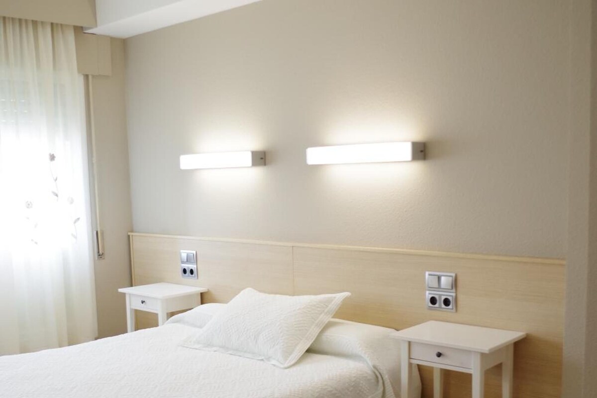 A hotel room with a large bed, two bedside tables, and wall-mounted lighting.