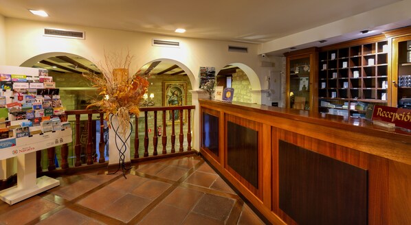 A reception area with a wooden reception desk, a bulletin board with magazines, and a decorative vase. - Palacio de Pujadas (Viana)