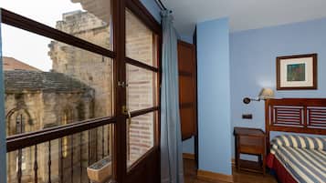 Un dormitorio con un ventanal grande, una cama de madera, una mesita de noche y un cuadro enmarcado en la pared.