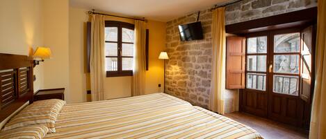 Una habitación de hotel con una cama, un televisor de pantalla plana montado en una pared de piedra y una ventana con cortinas.