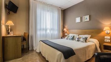 Habitación de hotel con cama, escritorio, silla, televisión y ventana con cortinas.