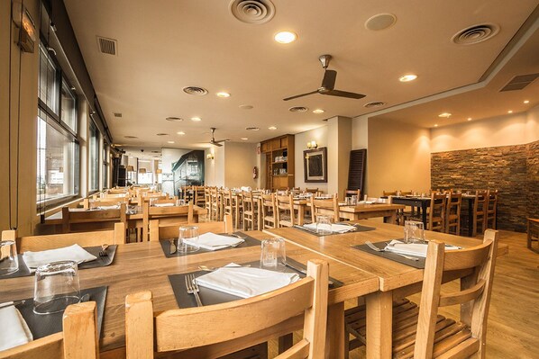 Un restaurant spacieux, doté de nombreuses tables et chaises en bois, de ventilateurs de plafond et de grandes fenêtres laissant entrer la lumière naturelle.